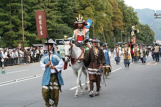 Un jinete disfrazado sobre un caballo blanco encabeza a acompañantes con trajes de época por una calle de Kioto durante el Jidai Matsuri